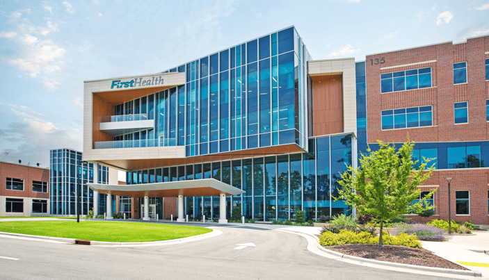 Modern glass building of FirstHealth with green lawn and trees. 